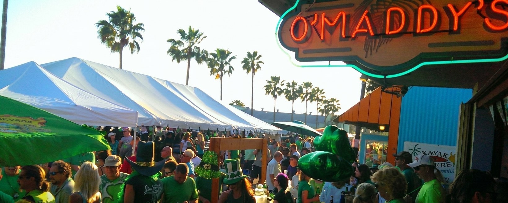 A crowd at O'Maddy's St. Patrick's Day street party under the neon sign