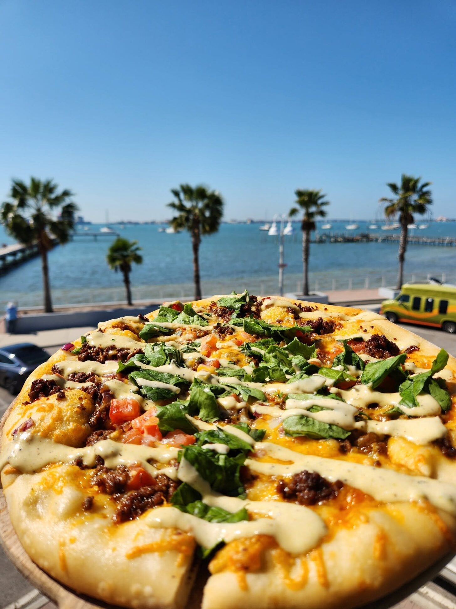 A loaded pizza with palms and sailboats behind